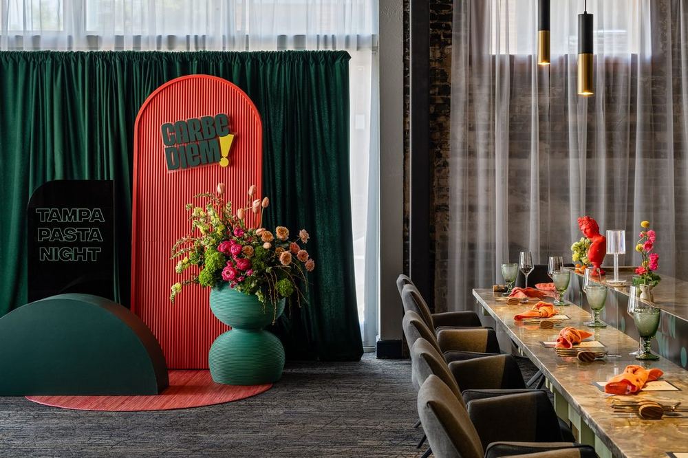Carbe Diem Tampa pasta night dining room with a green curtain backdrop, custom signage, and a long styled table
