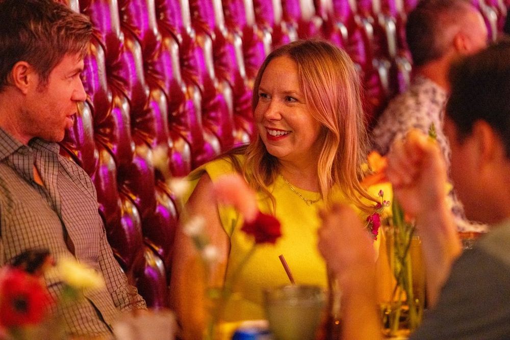 Guests laughing over dinner in a red tufted booth at the Carbe Diem takeover of Bar Dough, Denver