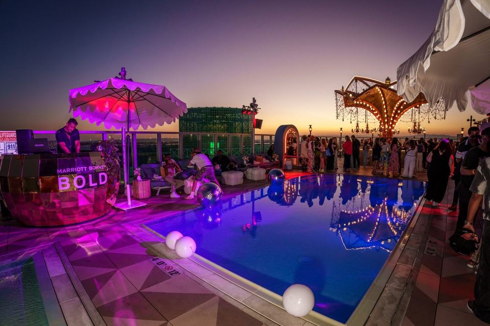 Marriott Bonvoy Bold rooftop pool party at sunset with guests, a DJ, and purple lighting